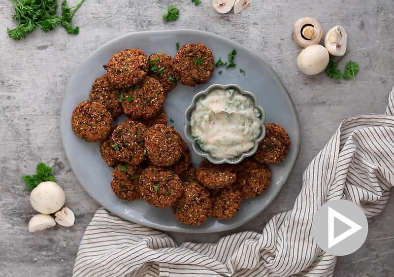 Talíř s houbovými karbanátky a dipem, obklopený čerstvými houbami a petrželkou na šedém povrchu