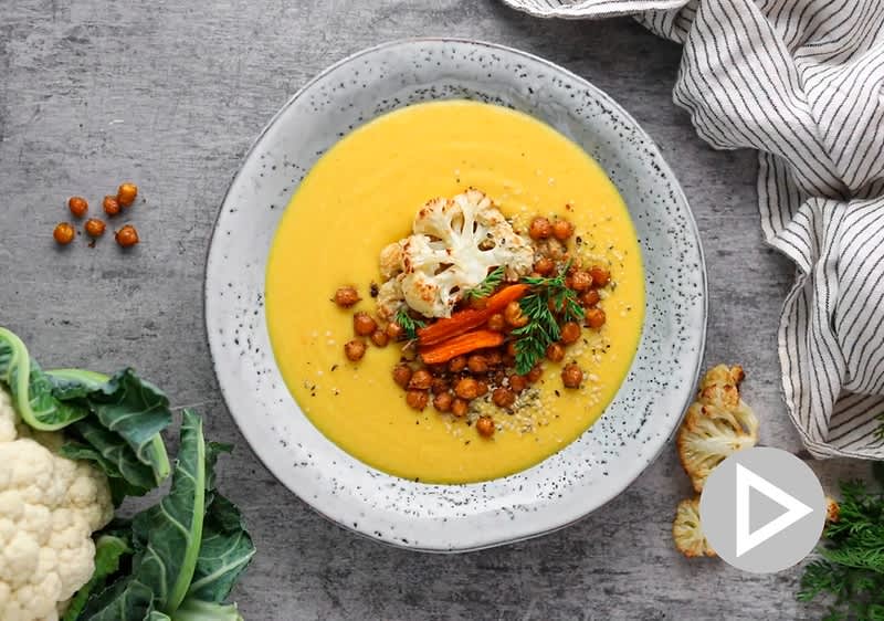 Polévka s pečenou zeleninou na šedém talíři, vedle květák a pruhovaná utěrka