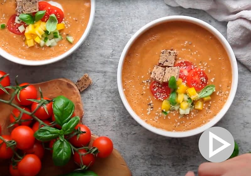 Rajčatová polévka s krutony, cherry rajčaty a bazalkou na stole, vedle čerstvá rajčata a bazalka