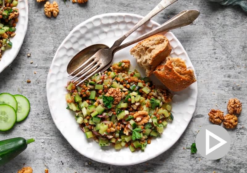 Talíř s bulgurem, okurkou, ořechy a chlebem na šedém povrchu