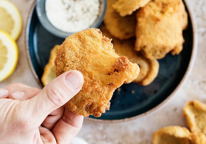 Smažené žampiony držené v ruce, talíř s dalšími žampiony a dipem.