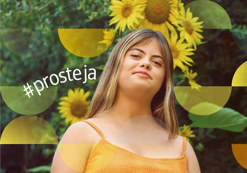Žena v oranžových šatech před slunečnicemi s nápisem #prosteja