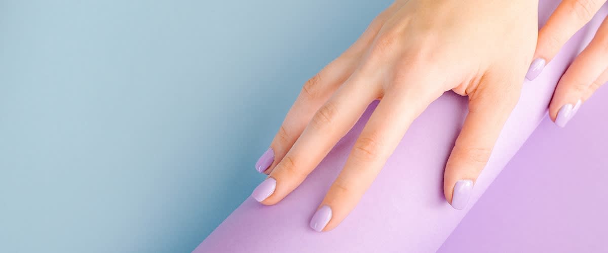 Ruka s fialovými nehty na fialovém a modrém pozadí