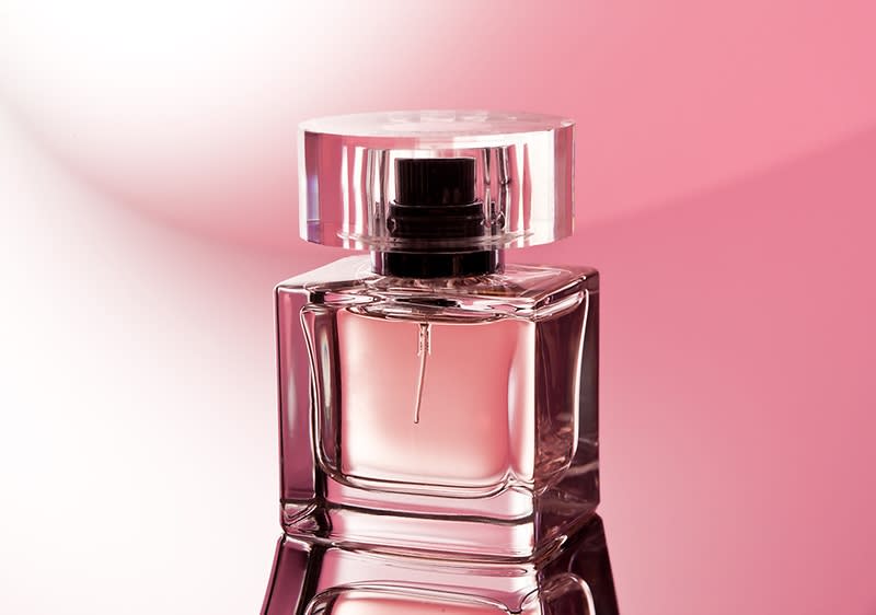 Skleněný flakon parfému na růžovém pozadí