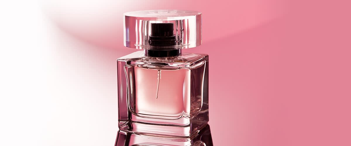 Skleněný flakon parfému na růžovém pozadí