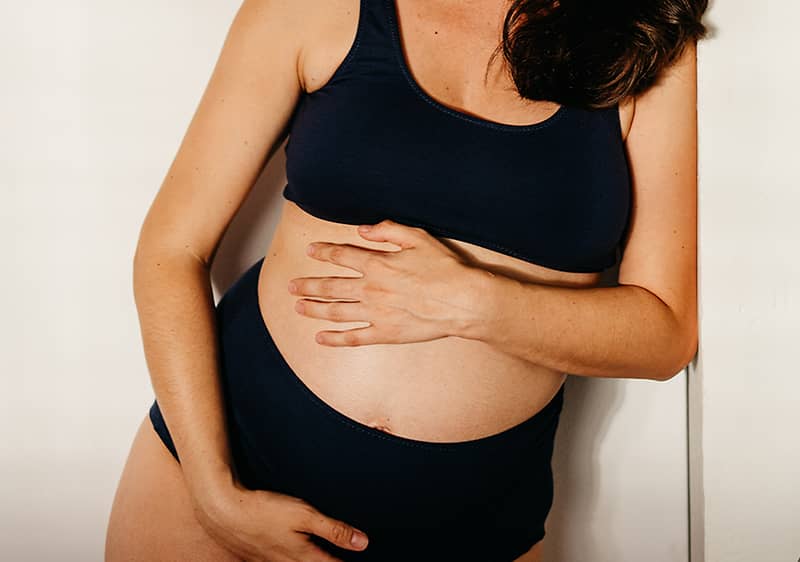 Těhotná žena v tmavém spodním prádle drží ruce na břiše