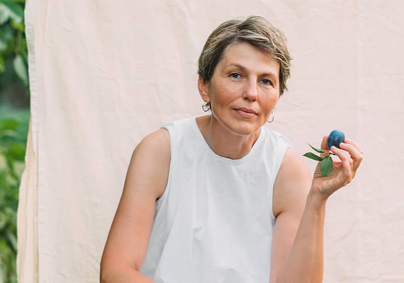 Osoba držící švestku před světlým pozadím a zelení v pozadí