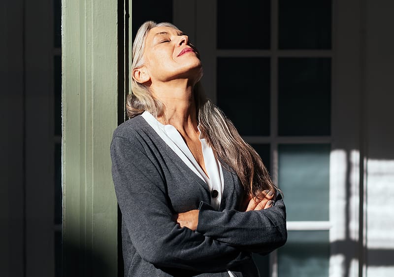 Žena s šedými vlasy opřená o sloup