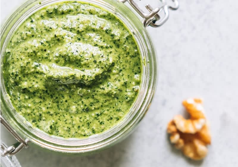 Sklenice s domácím bazalkovým pestem a vlašský ořech na bílém povrchu