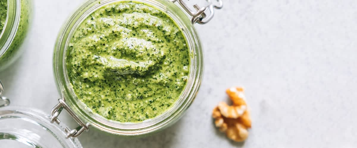 Sklenice s domácím bazalkovým pestem a vlašský ořech na bílém povrchu