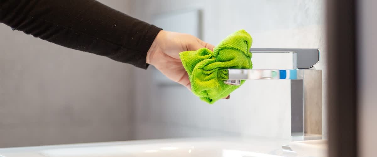 Čištění vodovodní baterie zeleným hadříkem v koupelně