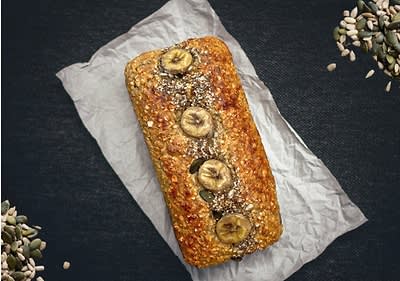 Banánový chlebíček na pečicím papíru s posypem semínek na tmavém pozadí