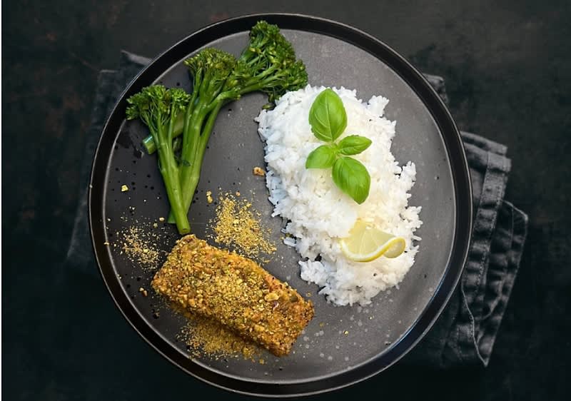 Talíř s brokolicí, rýží, citronem a obaleným kouskem ryby na tmavém pozadí