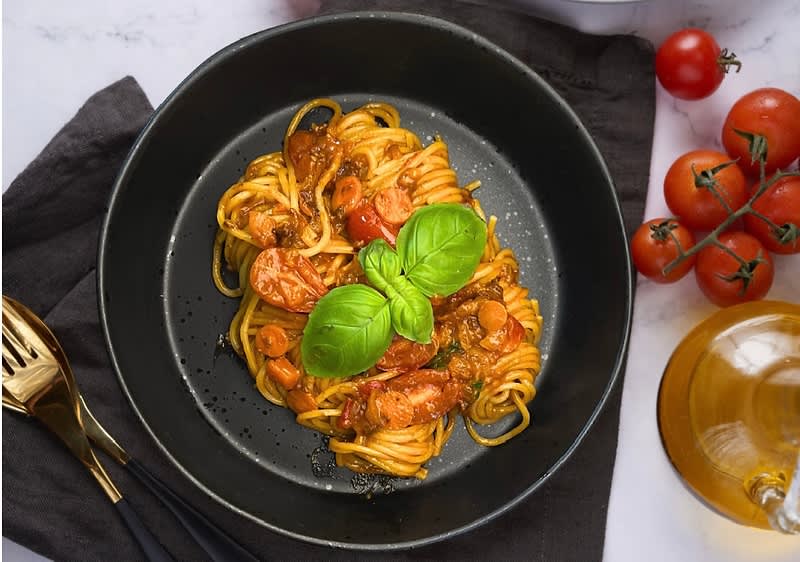 Špagety s rajčatovou omáčkou a bazalkou na talíři, vedle rajčata a olivový olej