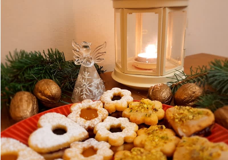 Vánoční cukroví na talíři, svíčka v lucerně, skleněný anděl, ořechy a větvičky jako dekorace