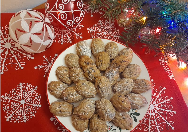 Vánoční cukroví na talíři, ozdobné koule, větvička s vánočními světly na červeném ubrusu.