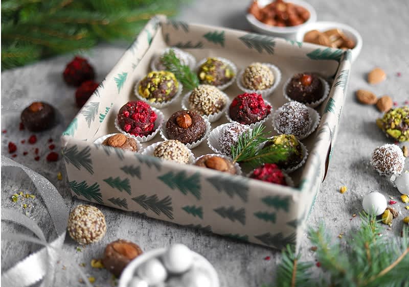 Vánoční krabička s různými druhy domácích cukrovinek na šedém povrchu s větvičkami a ořechy.