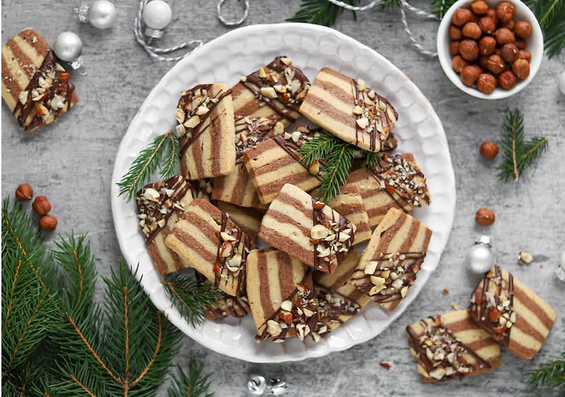Talíř s pruhovanými sušenkami, oříšky a větvičkami jehličnanů na šedém pozadí