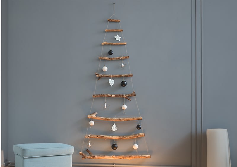 Minimalistický vánoční stromek z větví na šedé zdi s ozdobami