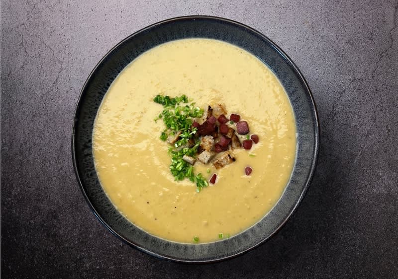 Krémová polévka v misce s kousky slaniny a zelenou petrželkou na vrchu