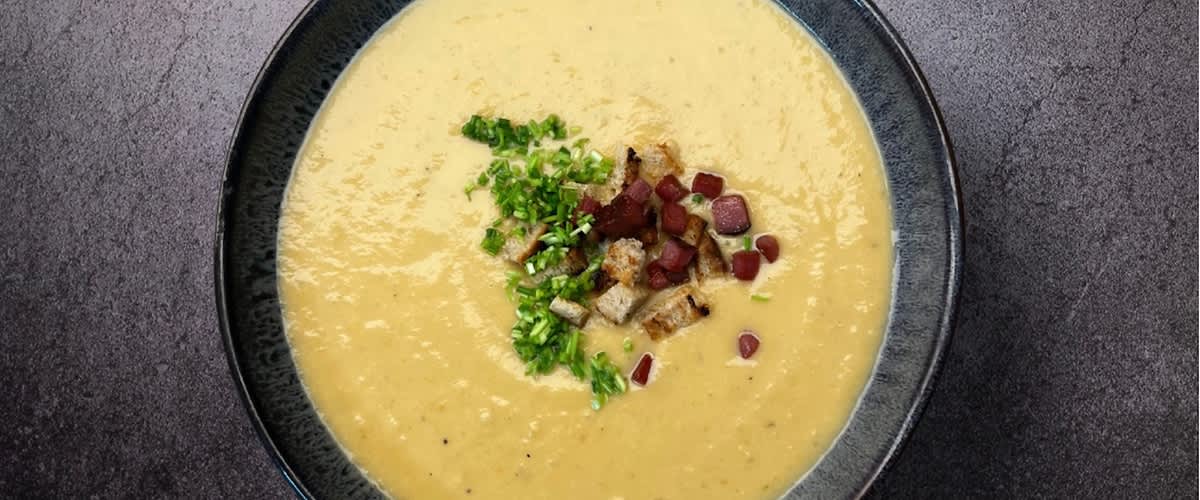 Krémová polévka v misce s kousky slaniny a zelenou petrželkou na vrchu