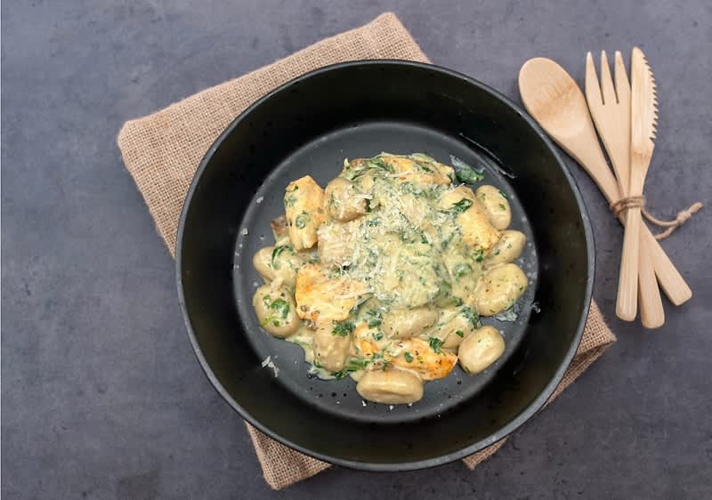 Těstoviny s krémovou omáčkou a kuřecím masem na černém talíři, vedle dřevěné příbory na jutové podložce