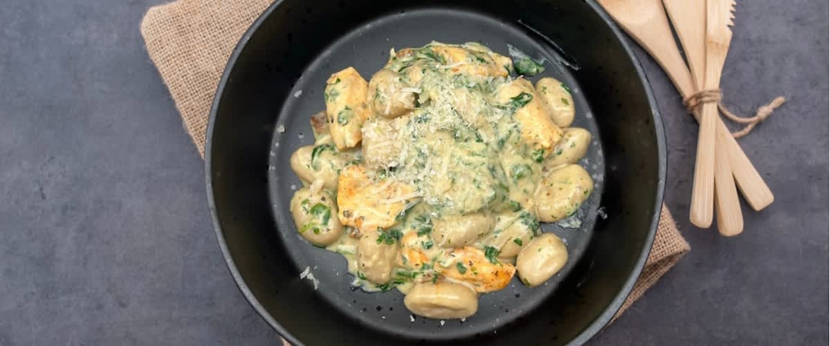 Těstoviny s krémovou omáčkou a kuřecím masem na černém talíři, vedle dřevěné příbory na jutové podložce