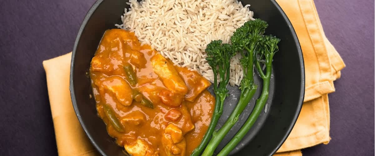 Kuřecí kari s rýží a brokolicí na černém talíři na žlutém ubrousku