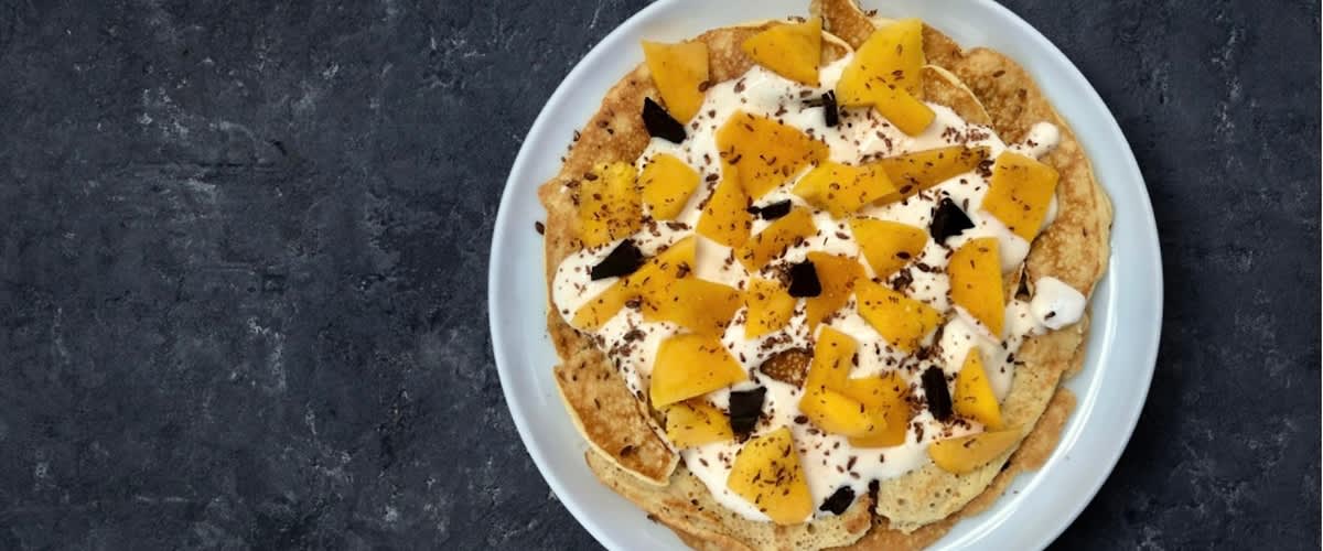 Palačinka s krémem, kousky manga a čokoládou na tmavém pozadí