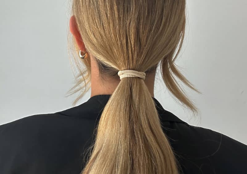 Žena s blond vlasy staženými do culíku, oblečená v černém oblečení, pohled zezadu.