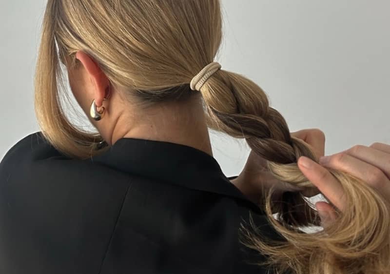 Žena s blond vlasy zapletenými do copu, oblečená v černém s náušnicemi