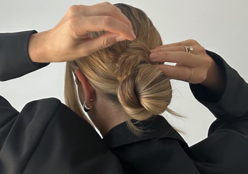 Žena upravující vlasy do elegantního drdolu, oblečená v černém sako.