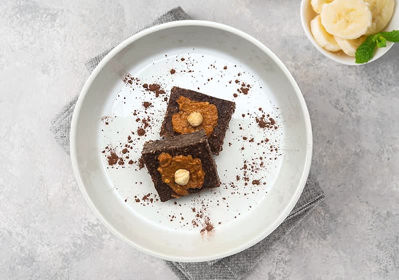 Čokoládové dezerty na talíři s oříšky, vedle misky s plátky banánu a lístkem máty.
