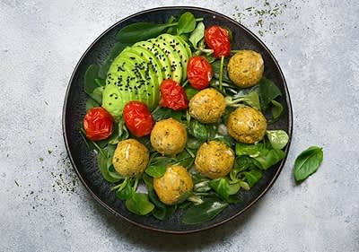 Talíř s avokádem, pečenými rajčaty, zelenými lístky a kuličkami falafelu posypanými černým sezamem