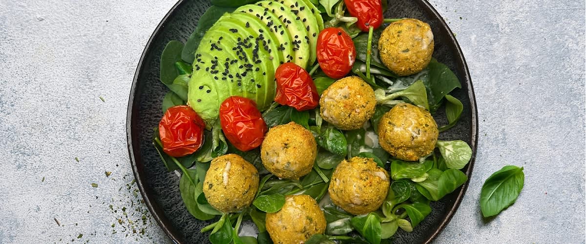 Talíř s avokádem, pečenými rajčaty, zelenými lístky a kuličkami falafelu posypanými černým sezamem