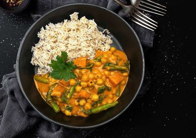 Talíř s kari z cizrny a zeleniny, podávaný s rýží, na tmavém pozadí.