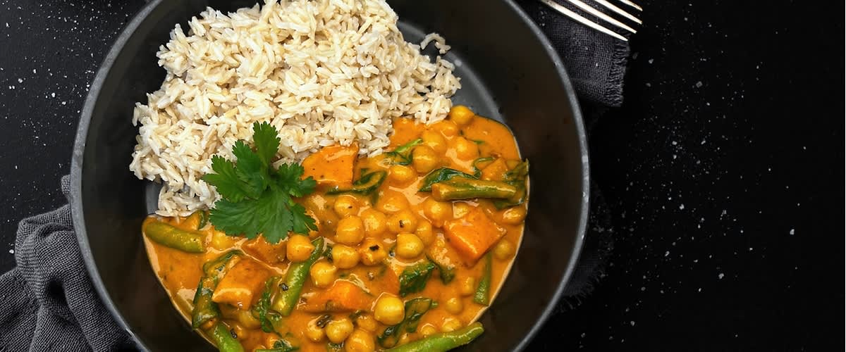 Talíř s kari z cizrny a zeleniny, podávaný s rýží, na tmavém pozadí.