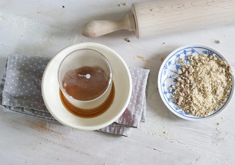 Sklenice s karamelem, miska s drcenými ořechy, váleček na těsto na bílém stole