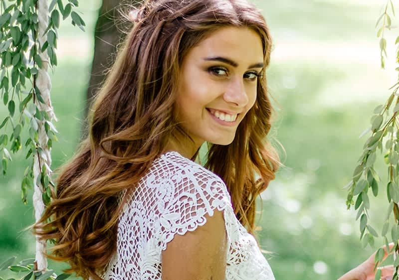 Žena v krajkových šatech stojící venku mezi zelenými větvemi