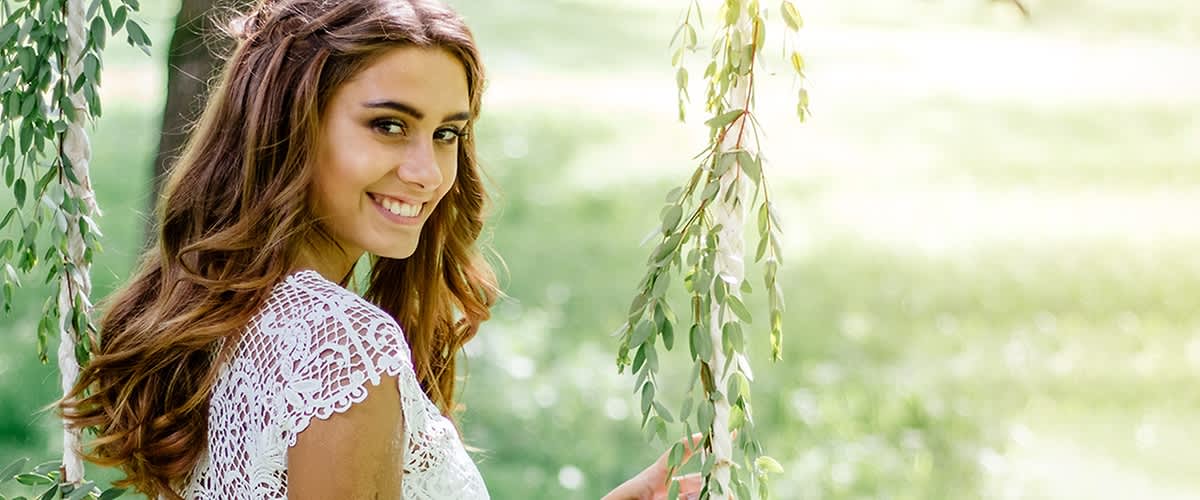 Žena v krajkových šatech stojící venku mezi zelenými větvemi