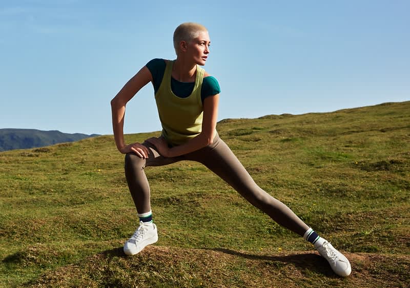 Osoba cvičící na travnatém kopci pod modrou oblohou