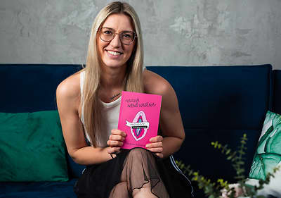 Žena sedící na pohovce drží růžovou knihu s nápisem Vulva není vagína