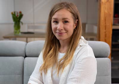 Žena sedící na šedé pohovce v moderním interiéru s květinami na stole v pozadí