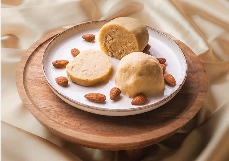 Marcipánové kuličky na talíři s mandlemi na dřevěném podnosu, pozadí z jemné látky