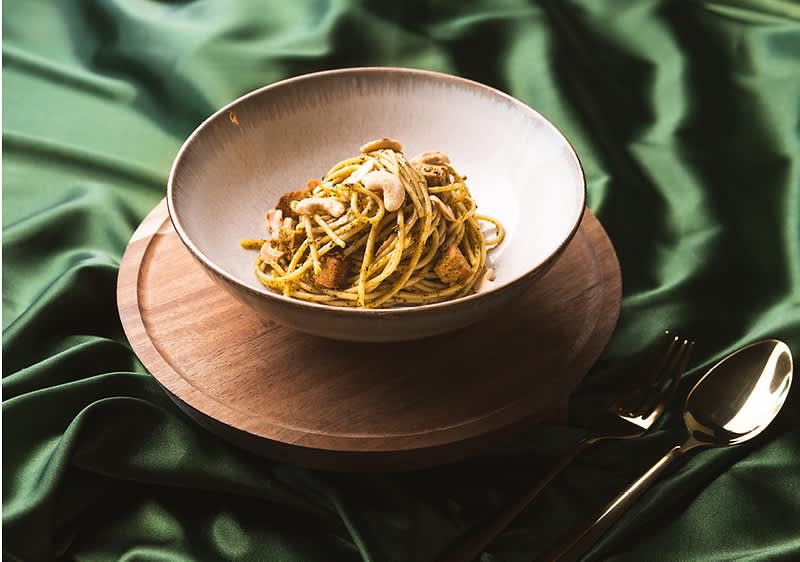 Těstoviny s houbami v bílé misce na dřevěném podnosu s zeleným saténovým ubrusem