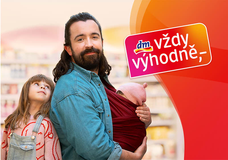 Muž s dítětem v šátku a dívka v obchodě, logo dm s textem vždy výhodně