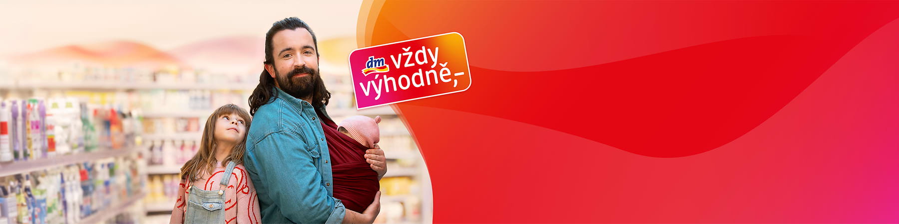 Muž s dítětem v šátku a dívka v obchodě, logo dm s textem vždy výhodně