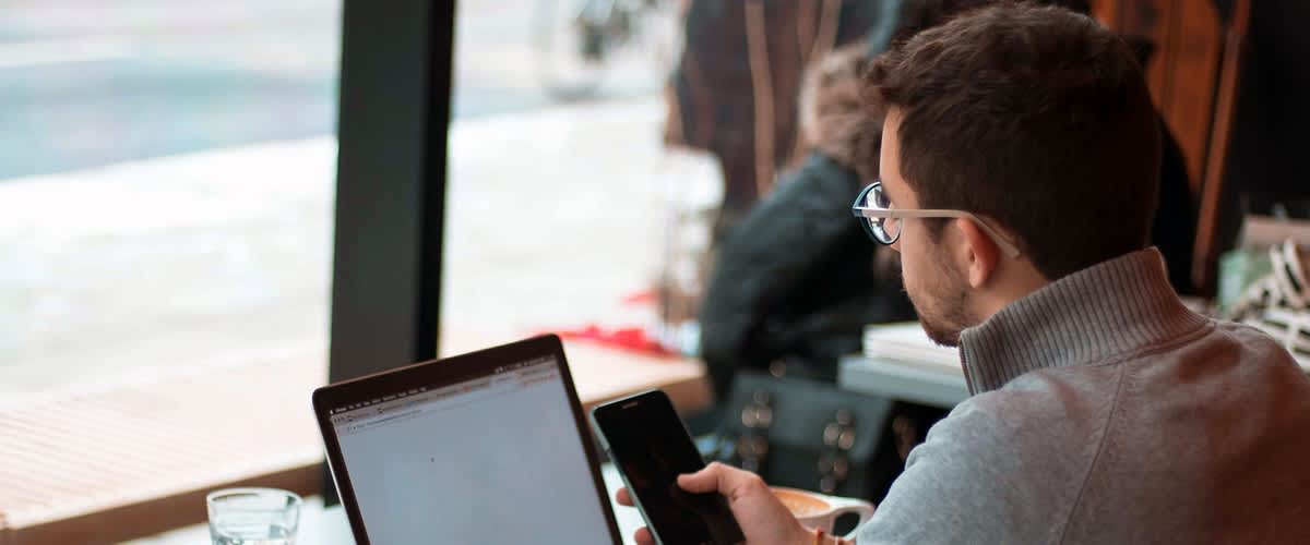 muž za počítačem se smartfonem v ruce