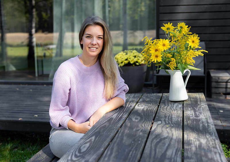 Žena sedící u dřevěného stolu s kyticí žlutých květin venku na terase.