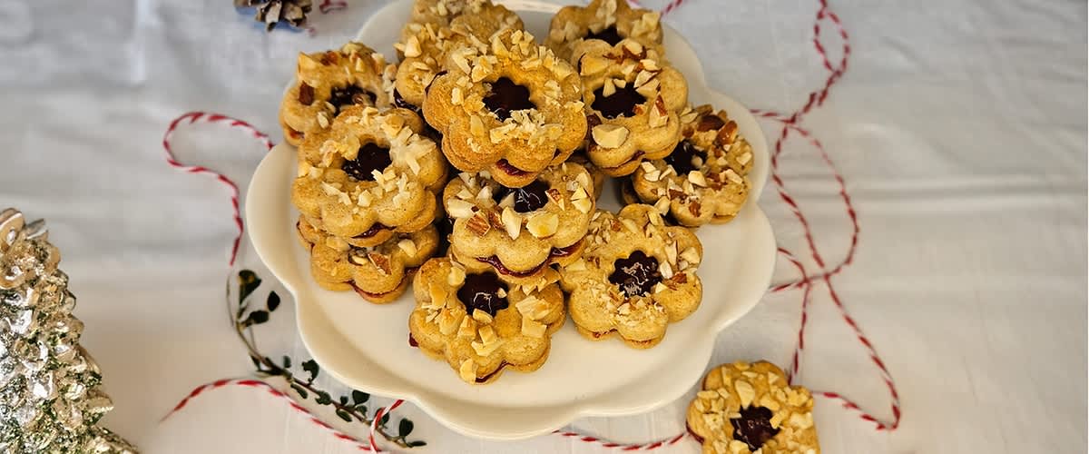 Talíř s vánočními cukrovinkami ve tvaru květin s marmeládou a oříšky na bílém ubrusu